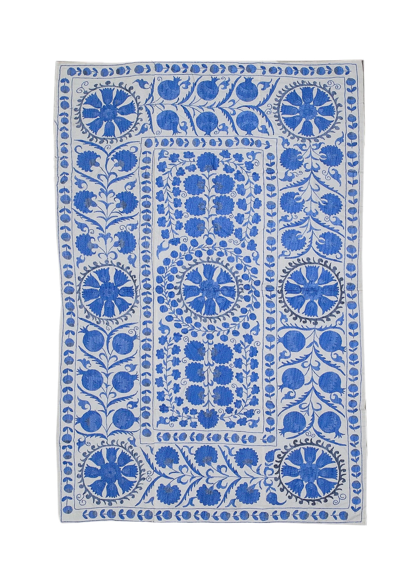 A rectangular Uzbek suzani featuring blue floral and pomegranate embroidery on a white cotton base.