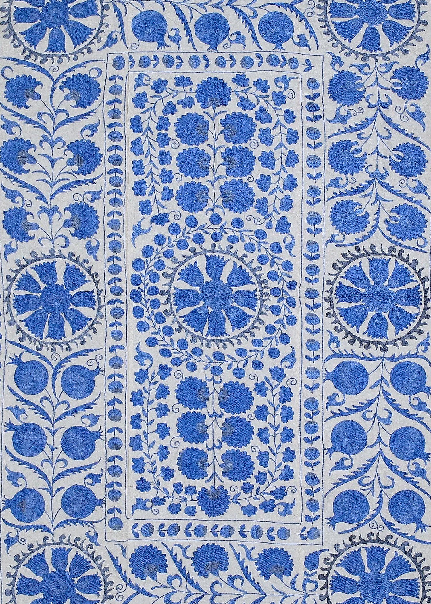 Hand-embroidered Uzbek suzani featuring blue floral and pomegranate motifs on a white cotton base.