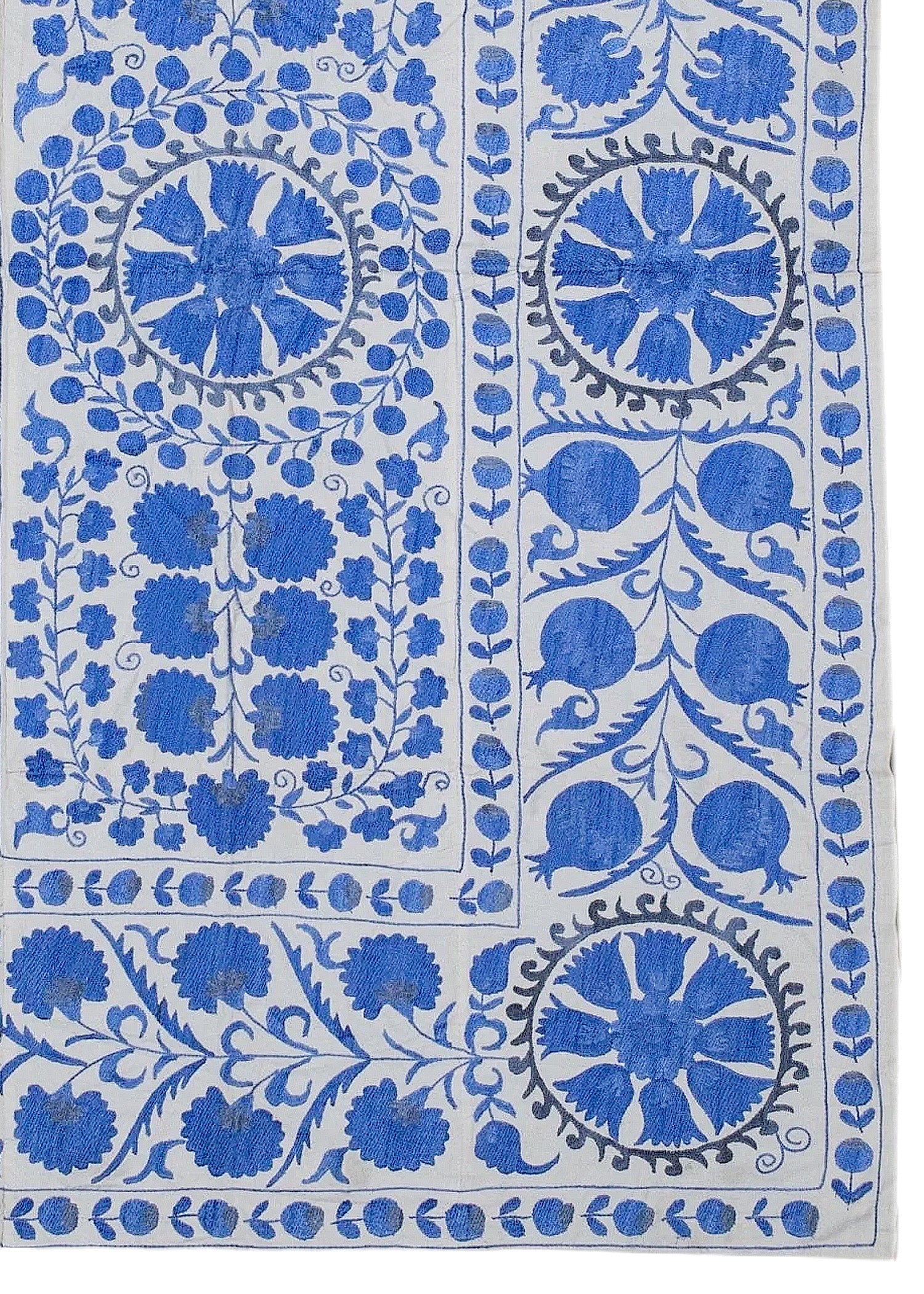 Hand-embroidered Uzbek Suzani featuring blue floral and pomegranate motifs on a white cotton base.