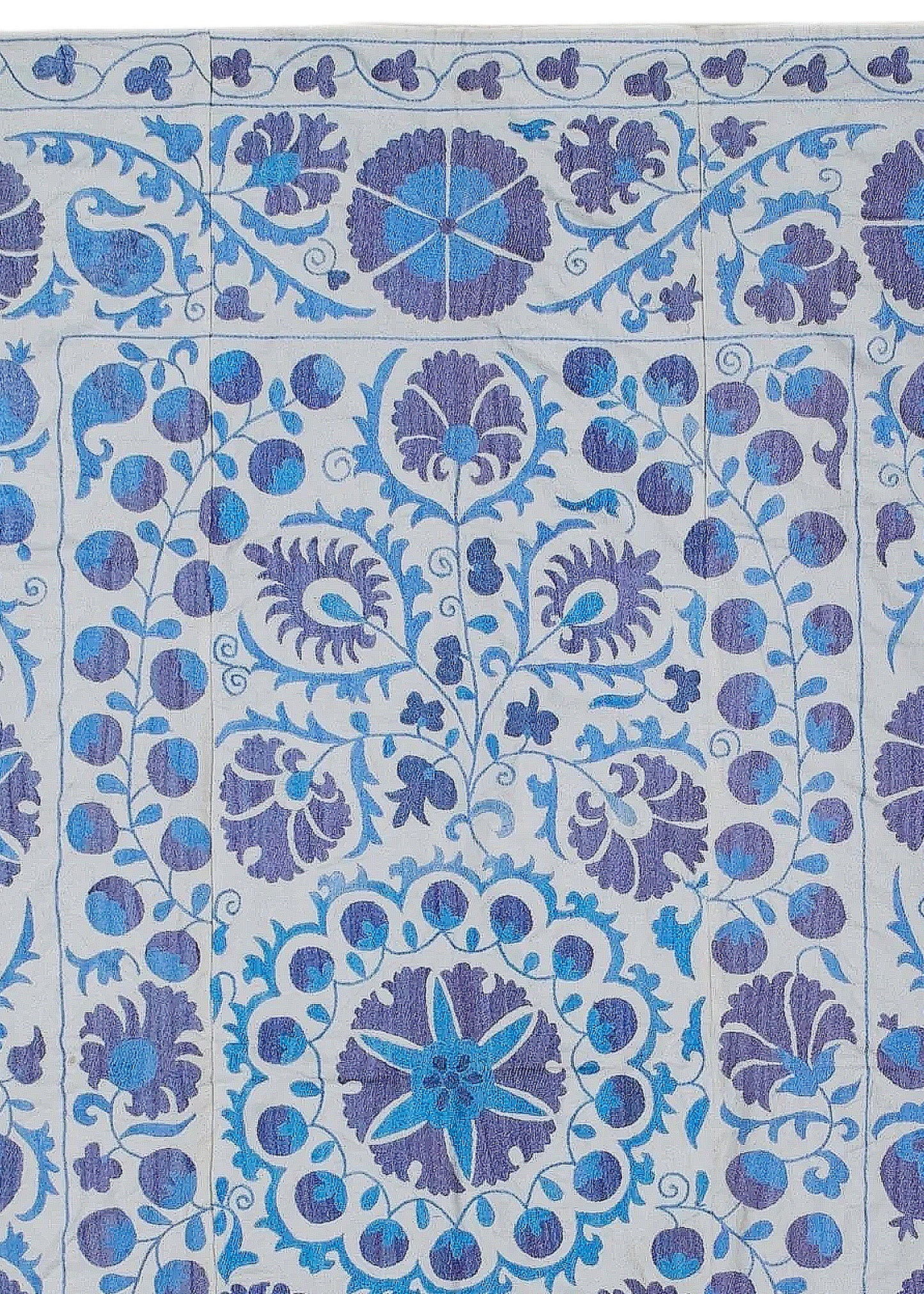 Hand-embroidered Uzbek Suzani textile featuring blue and purple floral motifs on a white background.