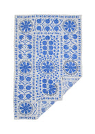 A rectangular Uzbek suzani featuring blue floral and pomegranate embroidery on a white cotton base.