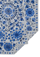 Hand-embroidered Uzbek Suzani featuring blue floral and pomegranate motifs on a white cotton base.