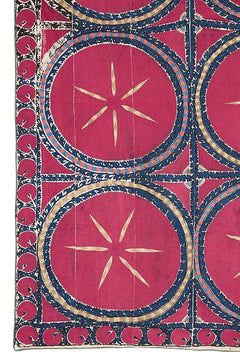 An antique silk Uzbek suzani featuring large circular celestial motifs in deep pink and blue.