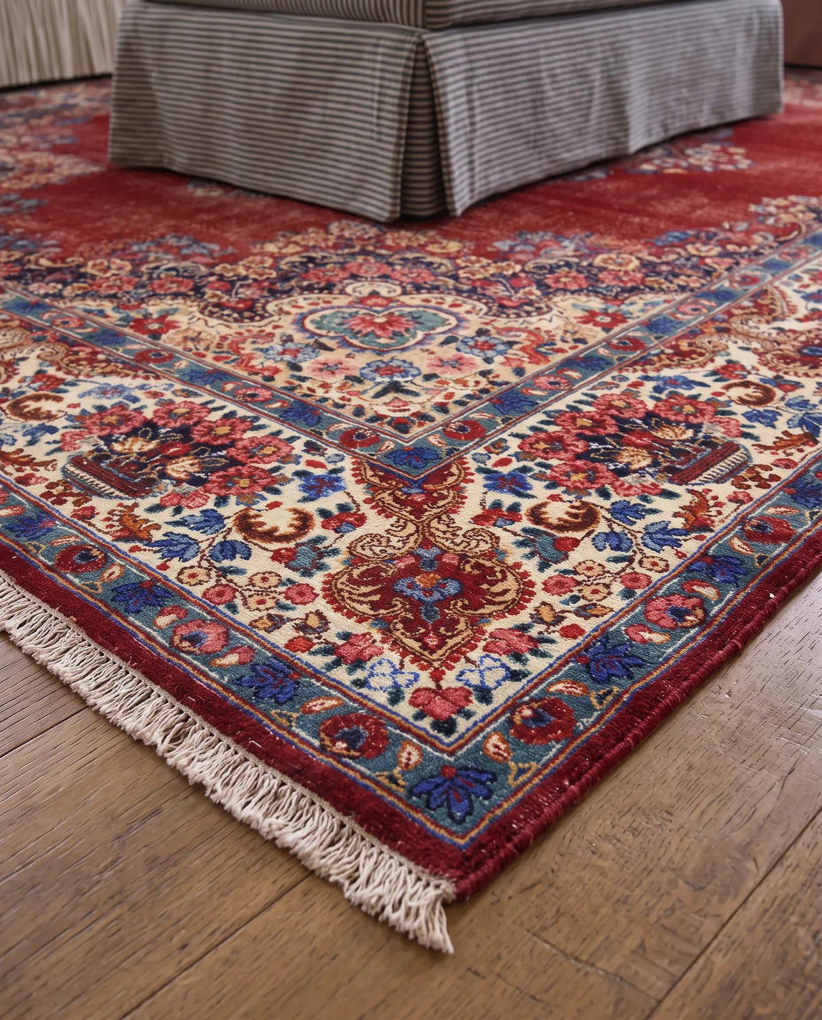 Hand-knotted vintage Persian Kerman wool rug with a red floral field, intricate blue medallion, and cream fringe.