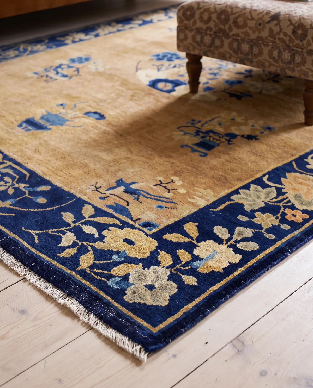 Hand-knotted antique Peking rug with a tan field, blue floral border, and traditional Chinese motifs on a timber floor.