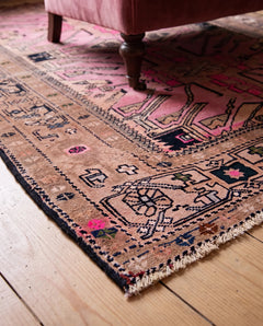 Vintage Caucasian Kazak rug with pink and brown geometric medallions, tribal motifs, and a short fringe on a wooden floor.
