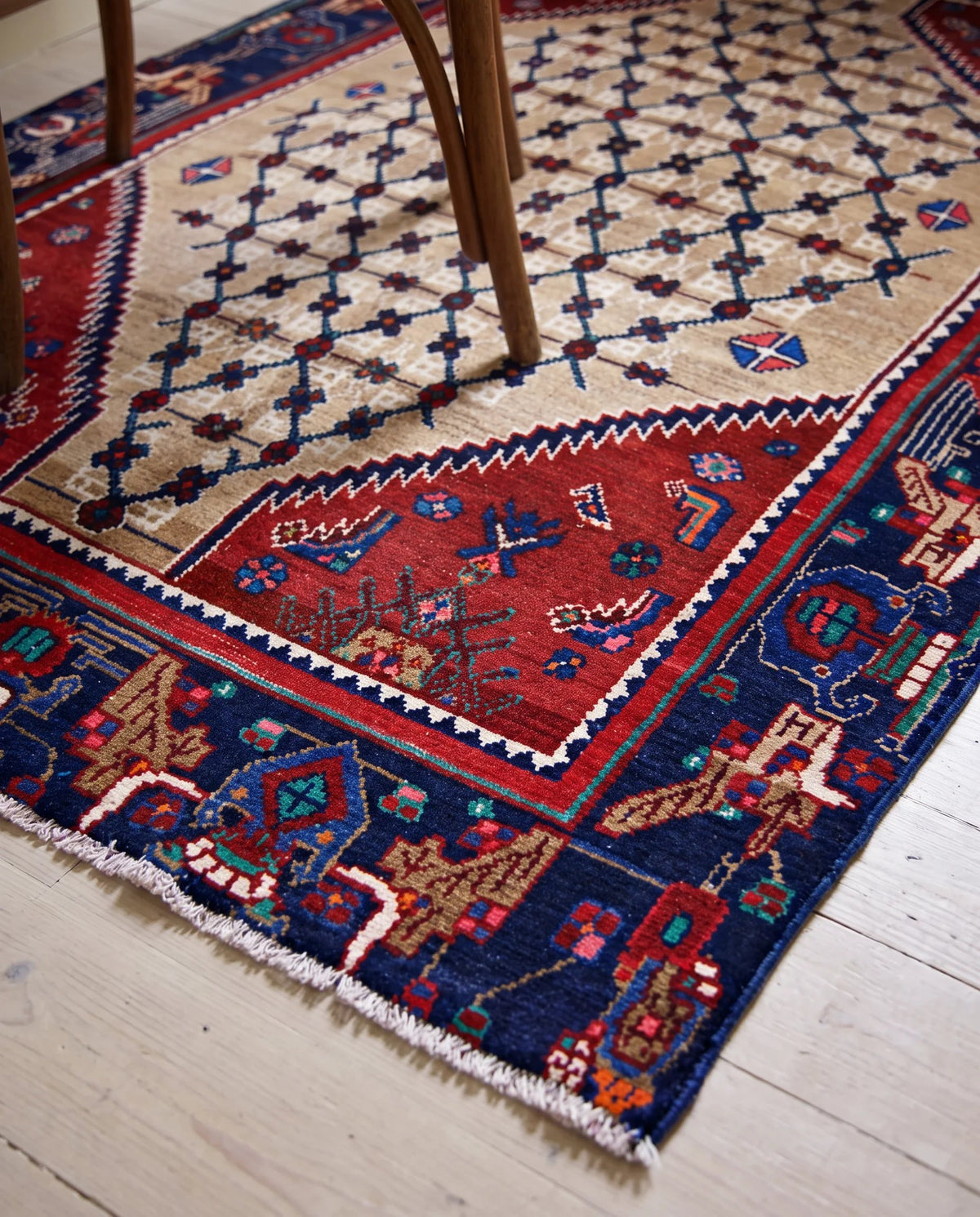 Vintage Persian Sanandaj rug featuring a beige lattice field, red accents, and a detailed blue border with fringe on a timber floor.