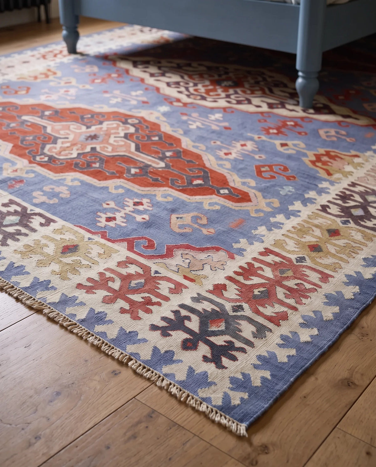 Vintage Serbian Pirot kilim with geometric folk patterns in blue, red, and cream on a wooden floor.