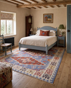 Vintage Serbian Pirot kilim with bold geometric patterns in blue, red, and cream, styled in a bedroom.