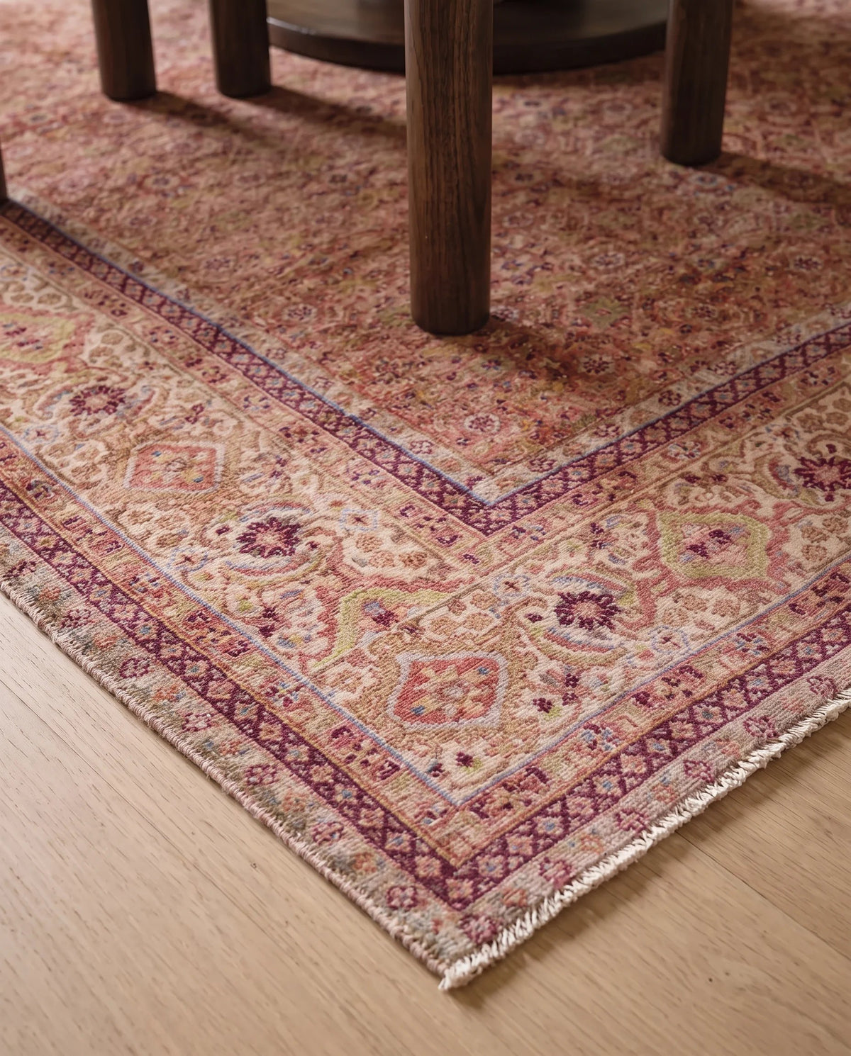 Vintage Persian Tabriz wool rug with intricate floral motifs in muted red, pink, and cream, featuring a fringed edge.