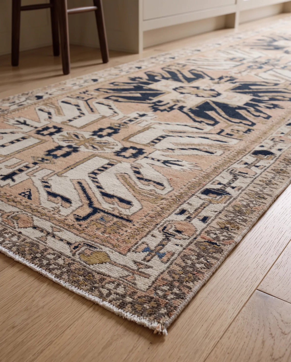 Vintage Caucasian Kazak runner with geometric navy and cream medallions on a soft peach field, laid on timber flooring.