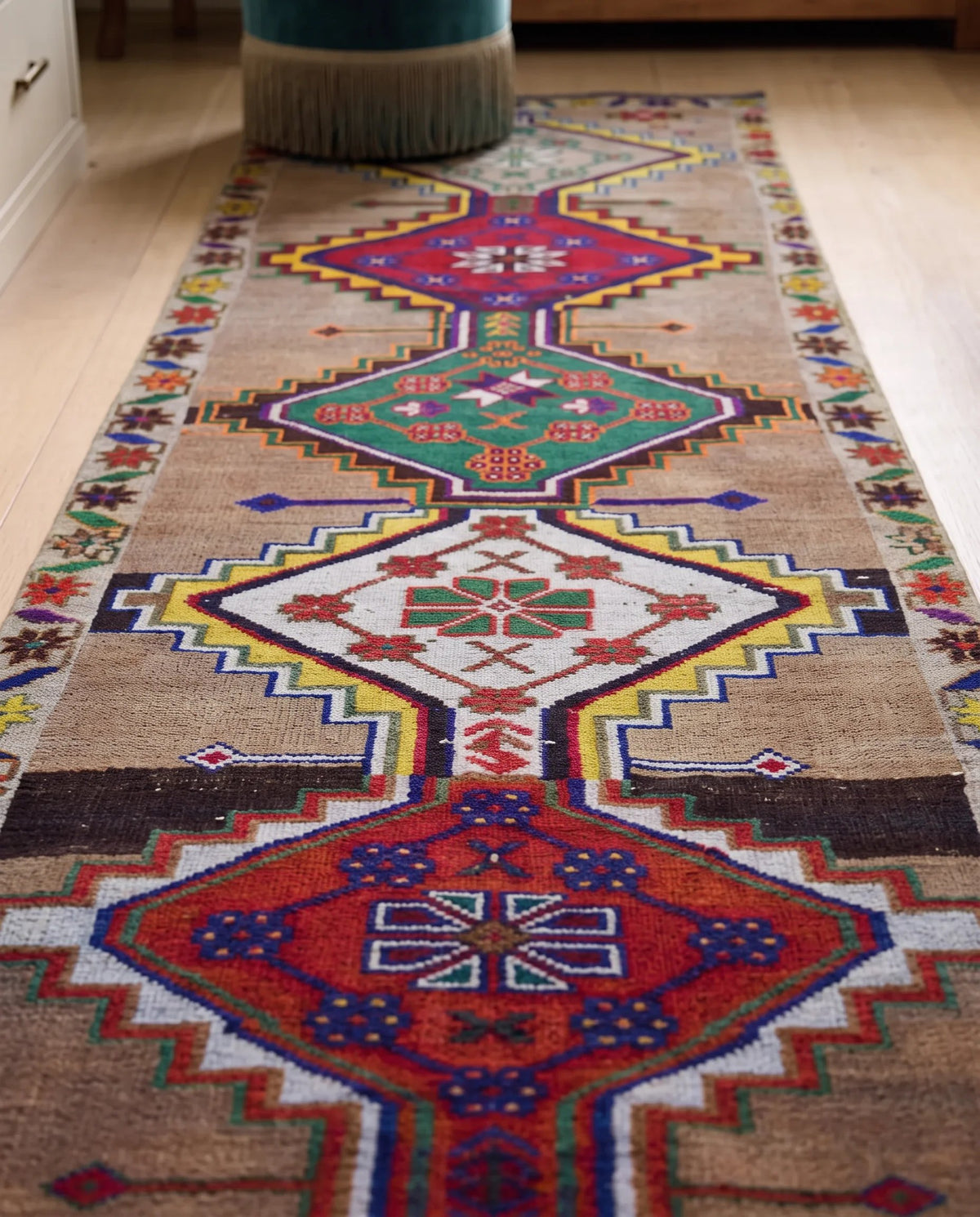 Vintage Kurdish Herki runner with bold geometric medallions in vibrant red, green, and yellow on a brown wool pile.