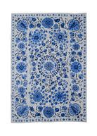A rectangular Uzbek suzani featuring intricate blue floral embroidery on a light cotton background.