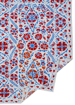 A white cotton textile featuring intricate hand-embroidered floral and botanical motifs in red and blue.