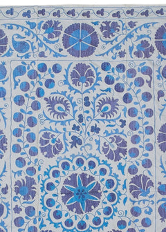 Hand-embroidered Uzbek Suzani textile featuring blue and purple floral motifs on a white background.