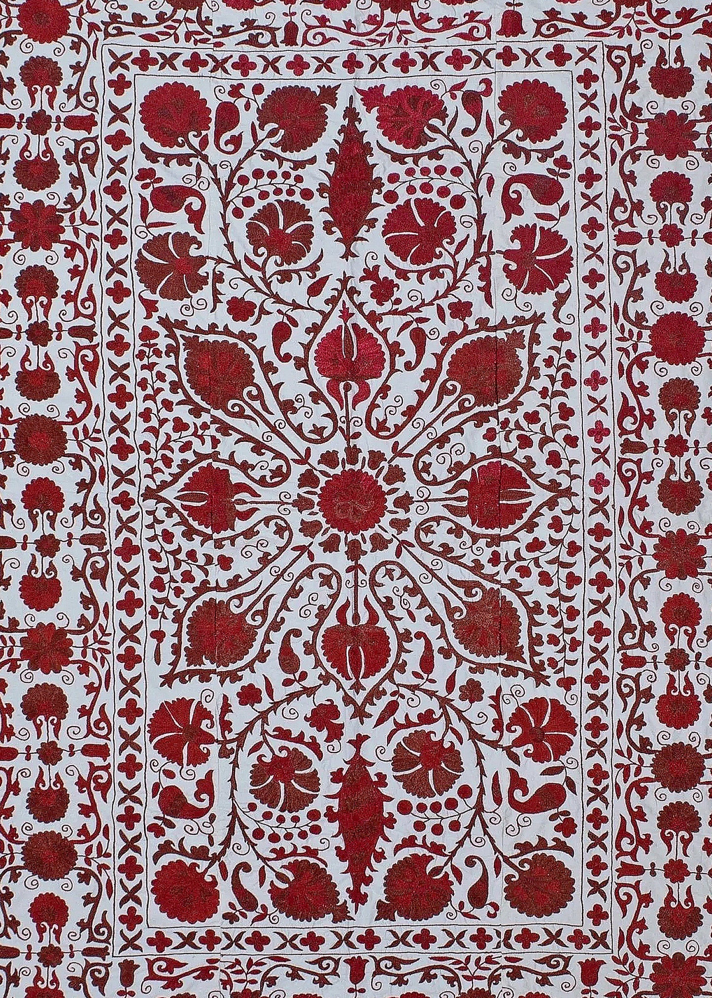 A hand-embroidered Uzbek suzani featuring intricate red floral motifs on a white cotton background.