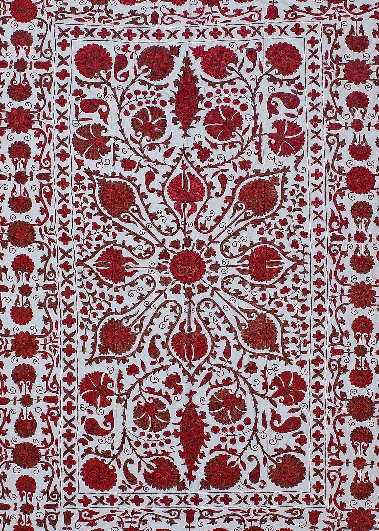 A hand-embroidered Uzbek suzani featuring intricate red floral motifs on a white cotton background.