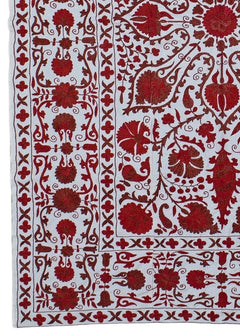 A hand-embroidered Uzbek Suzani featuring intricate red floral motifs on a white cotton base.