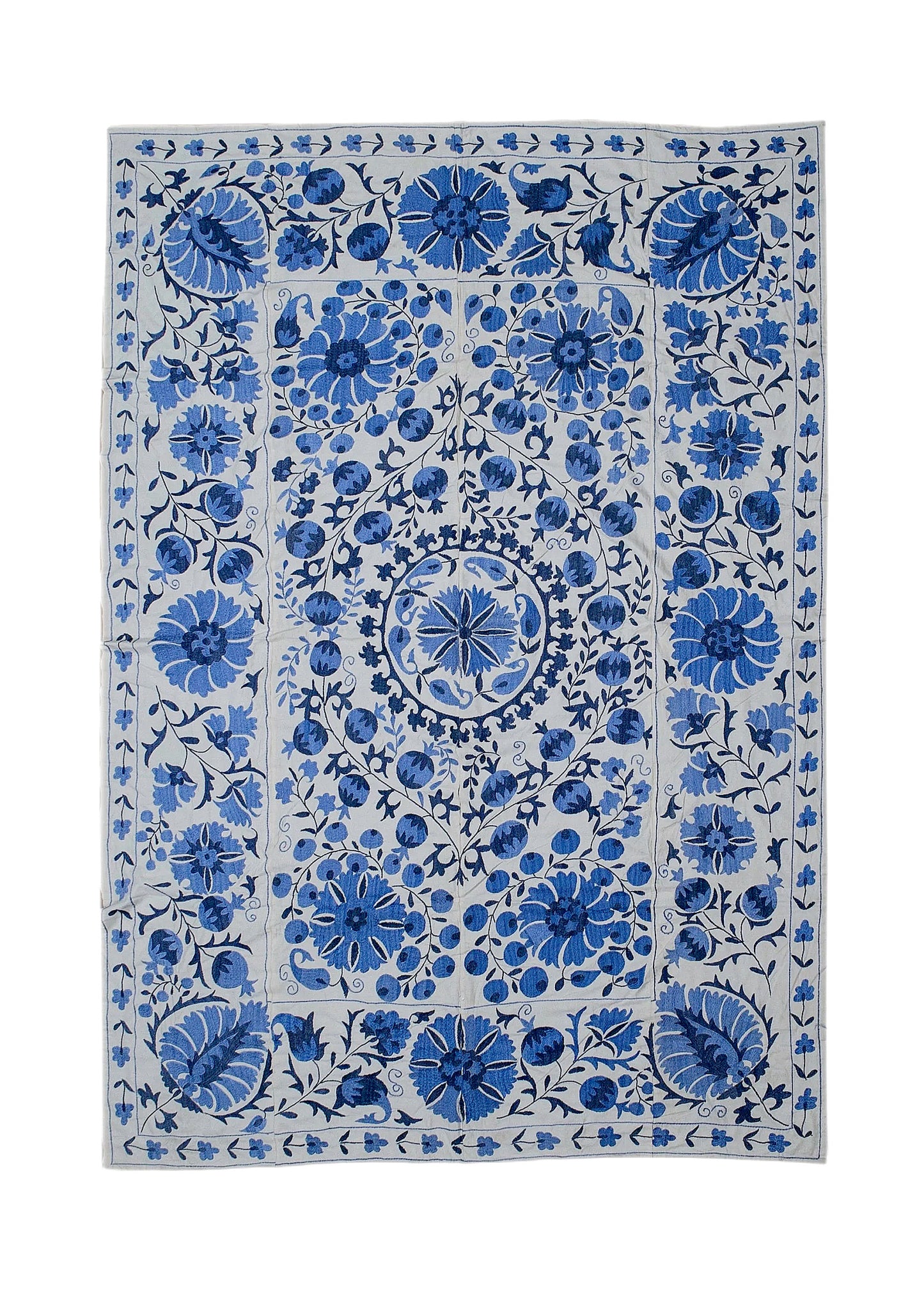 A rectangular Uzbek suzani featuring intricate blue floral embroidery on a light cotton background.