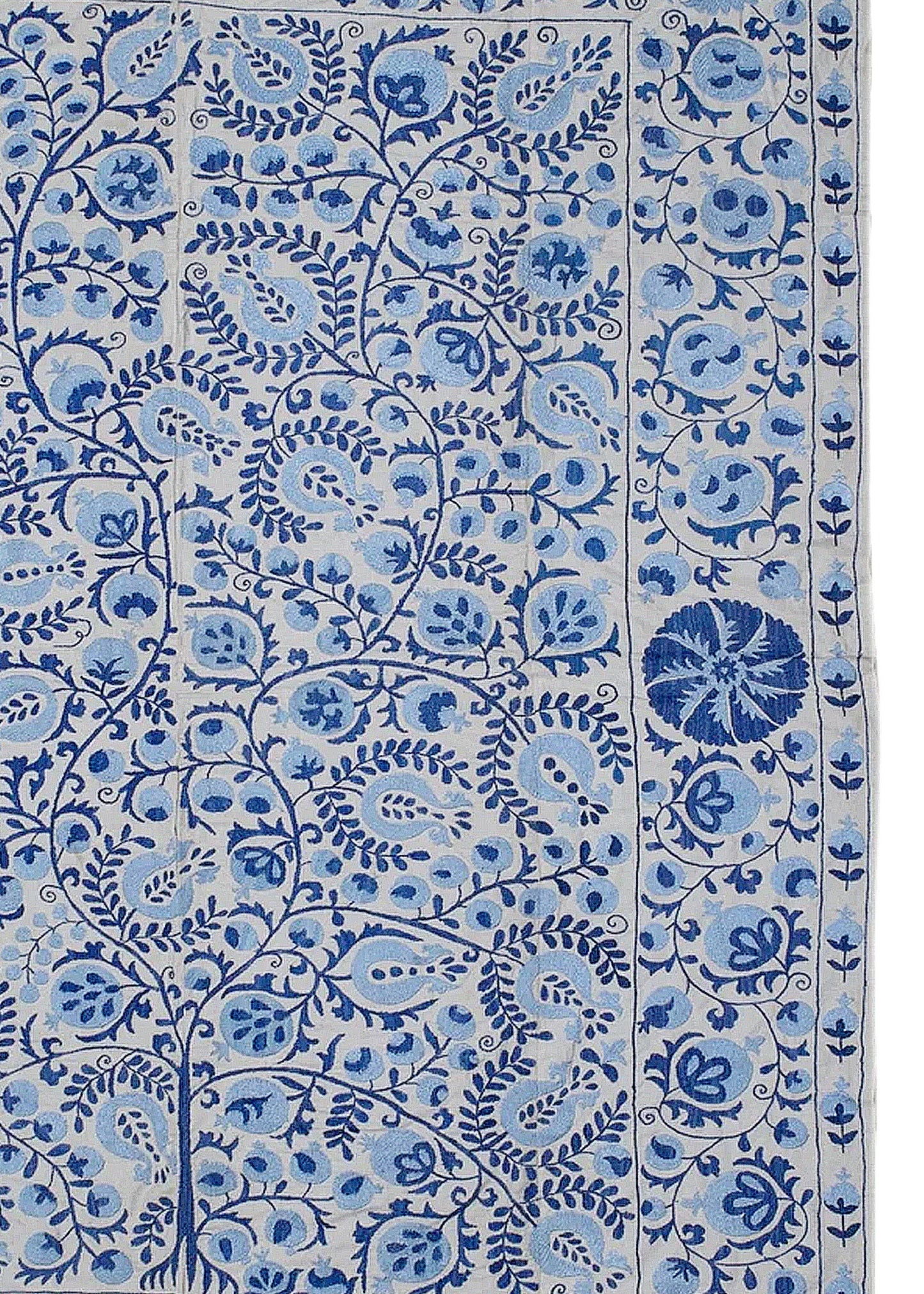 An Uzbek Suzani textile featuring intricate blue floral and pomegranate embroidery on a light base.