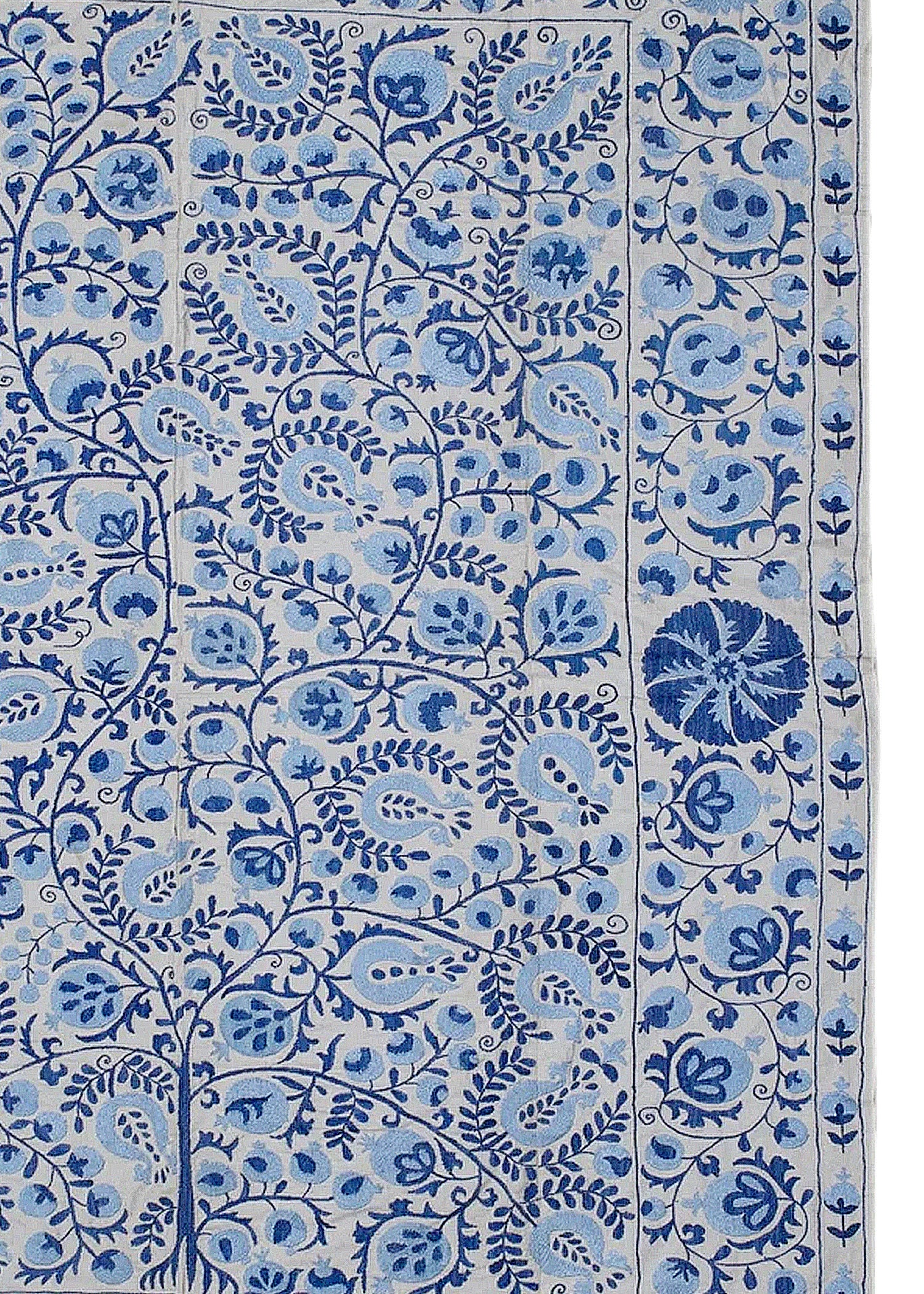 An Uzbek Suzani textile featuring intricate blue floral and pomegranate embroidery on a light base.