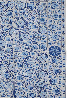 An Uzbek Suzani textile featuring intricate blue floral and pomegranate embroidery on a light base.
