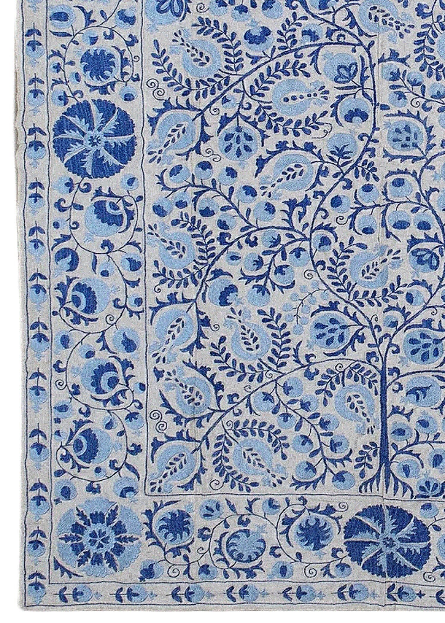 An Uzbek Suzani textile featuring intricate blue floral and pomegranate embroidery on a light base.