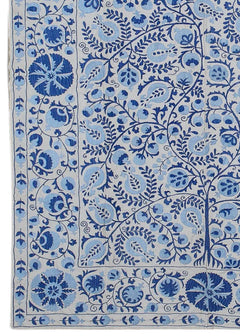 An Uzbek Suzani textile featuring intricate blue floral and pomegranate embroidery on a light base.