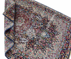 A vintage Persian Kerman rug featuring an intricate floral medallion design in blue and red tones.