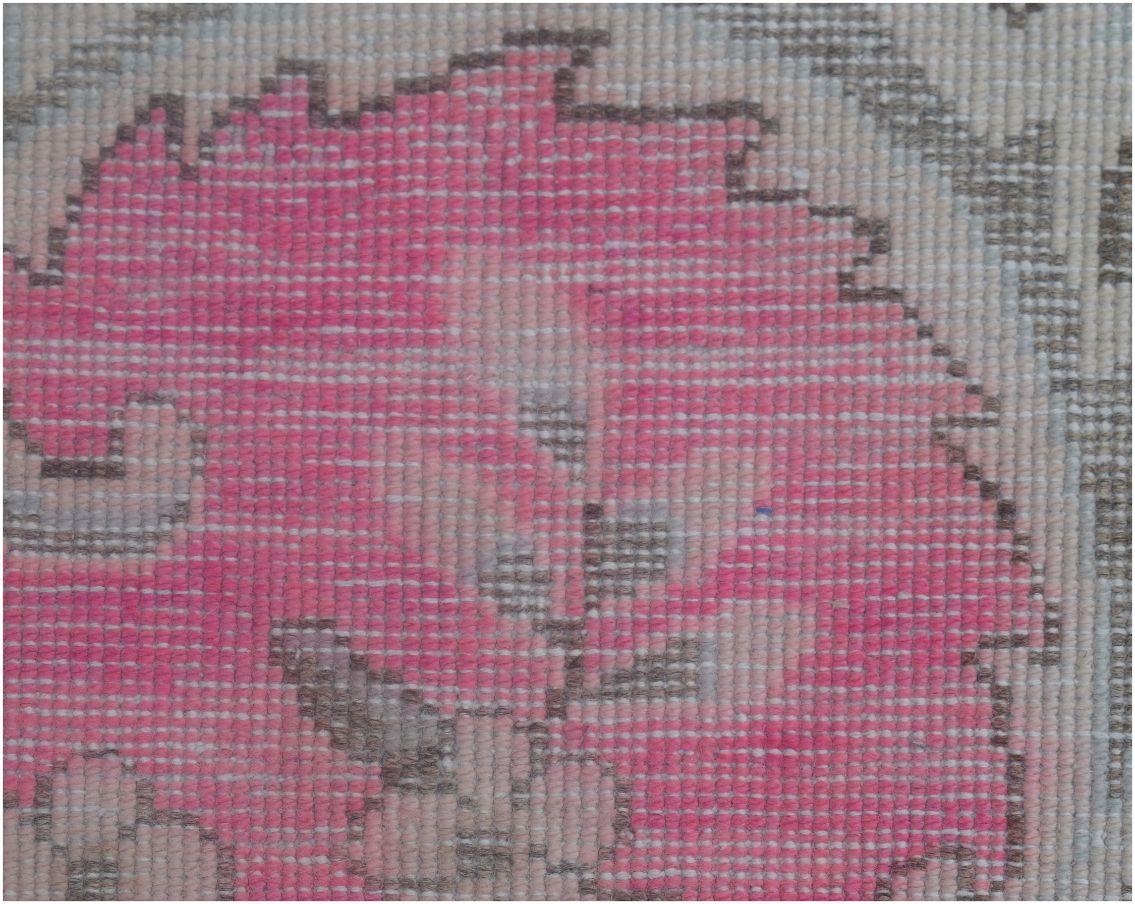 A close-up of a vintage Persian Kerman rug featuring a pink floral motif with intricate detailing.