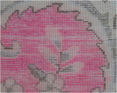 A close-up of a vintage Persian Kerman rug featuring a pink floral motif with intricate detailing.