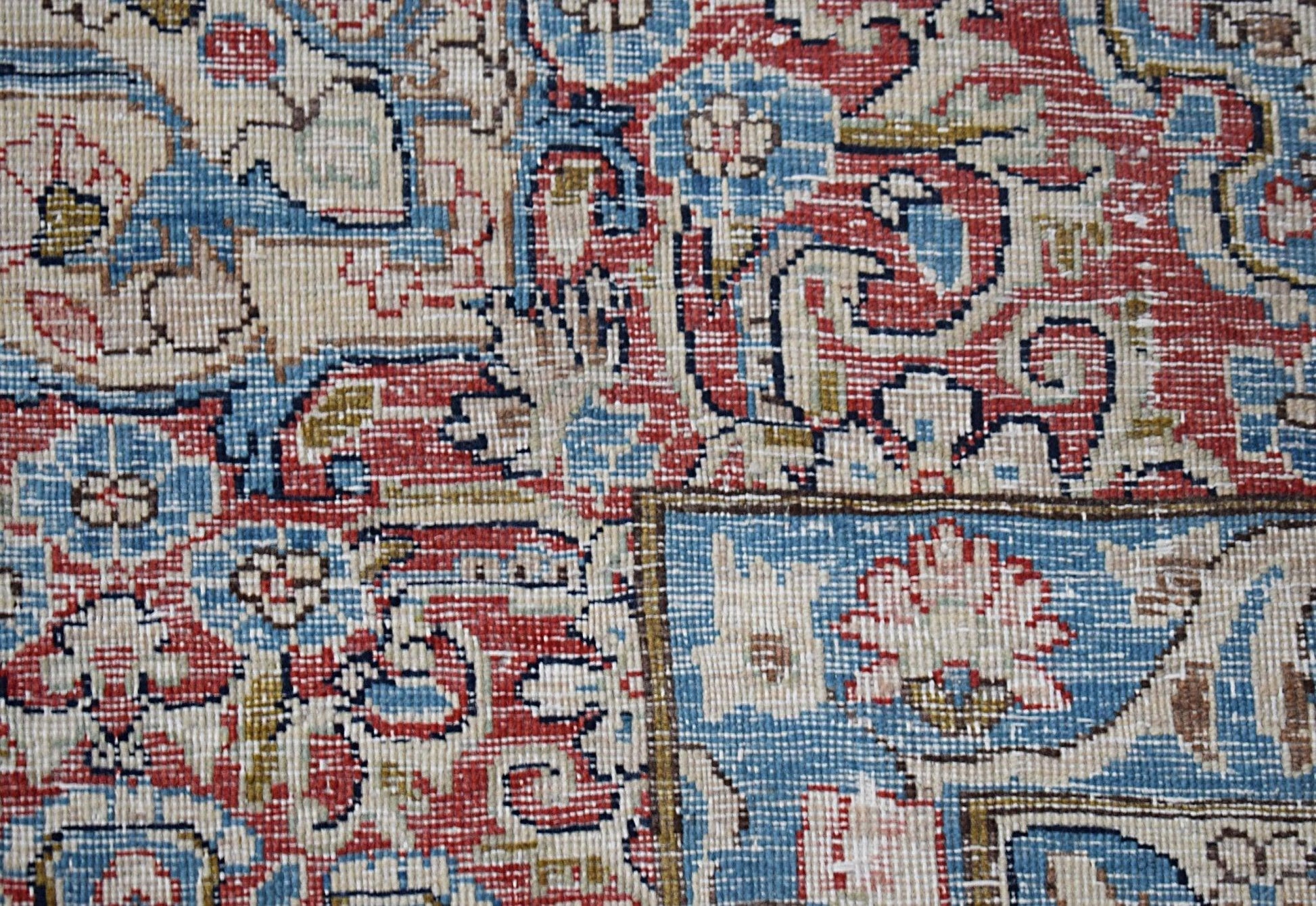 A close-up of a vintage Persian Kerman rug featuring intricate floral patterns in red and blue.