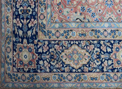 A vintage Persian Kerman rug featuring an intricate floral pattern in blue, pink, and cream tones.