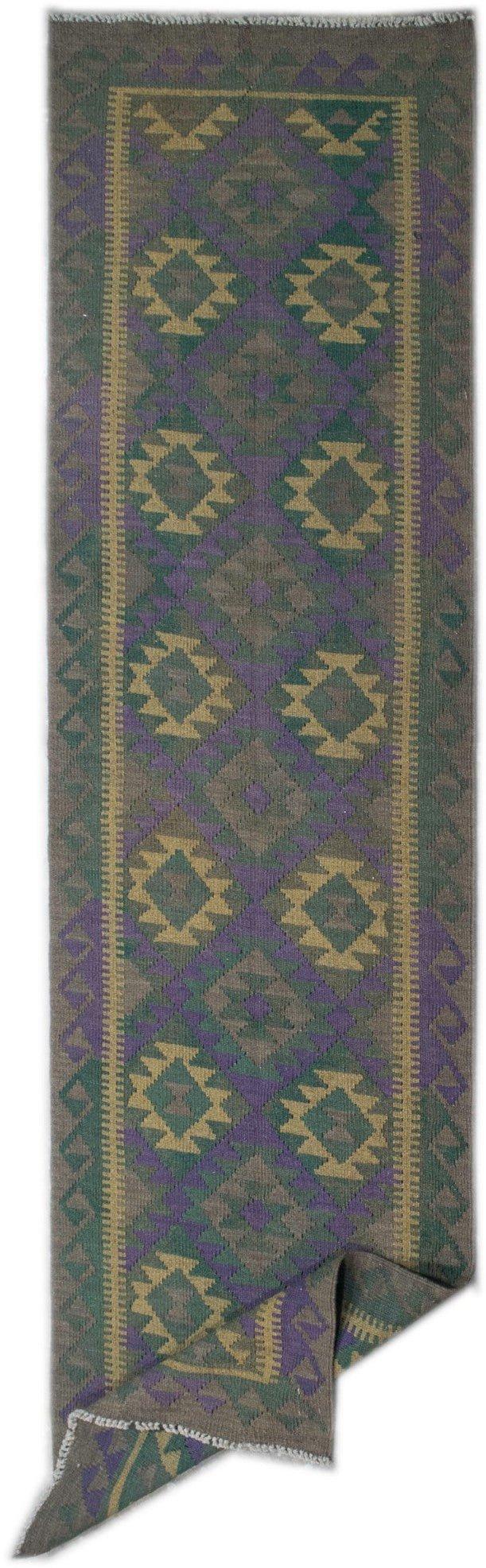 A handmade Afghan Maimana wool runner rug featuring a geometric pattern in green, purple, and tan.