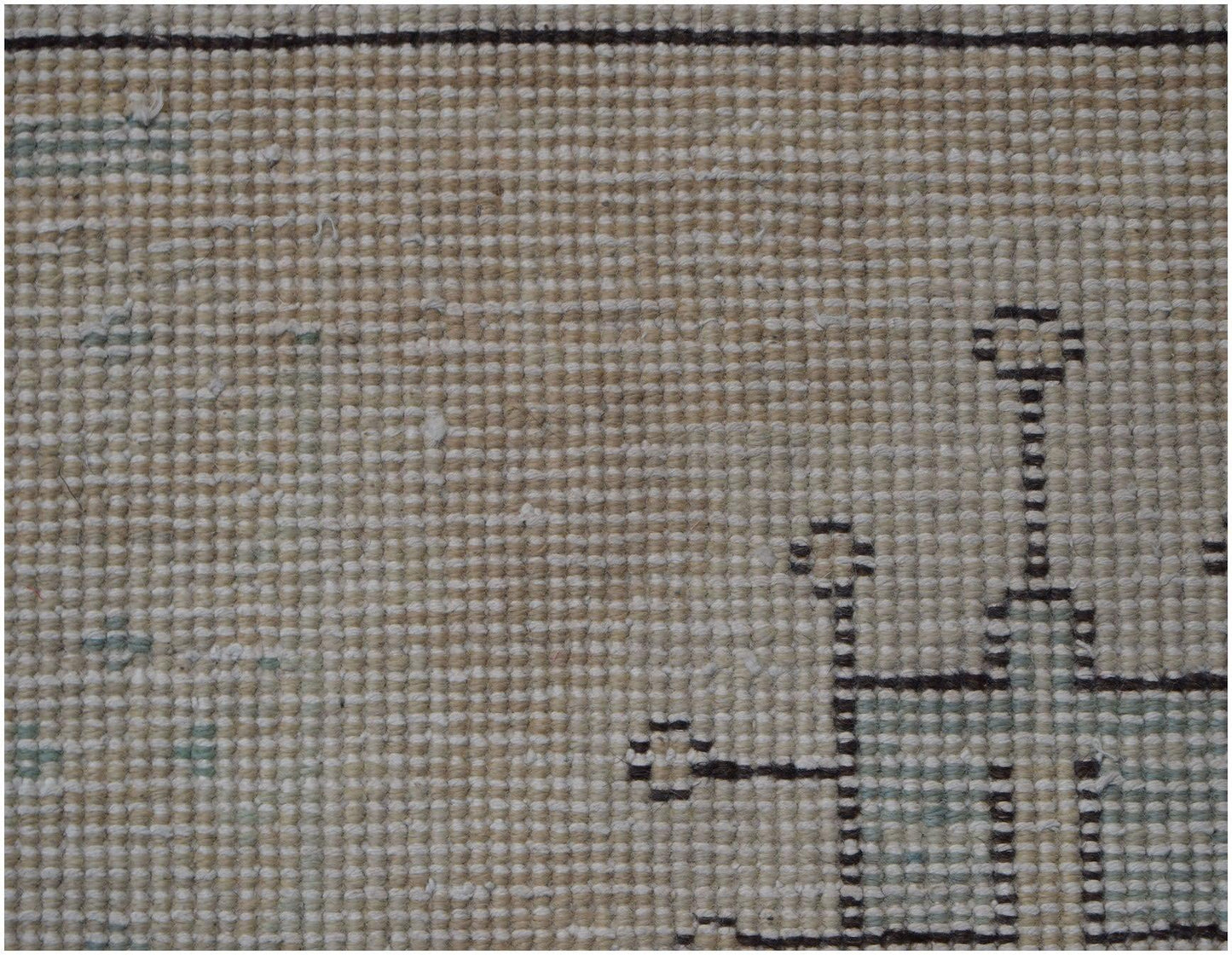 A close-up view of a vintage Persian Kerman rug featuring a geometric pattern on a beige field.