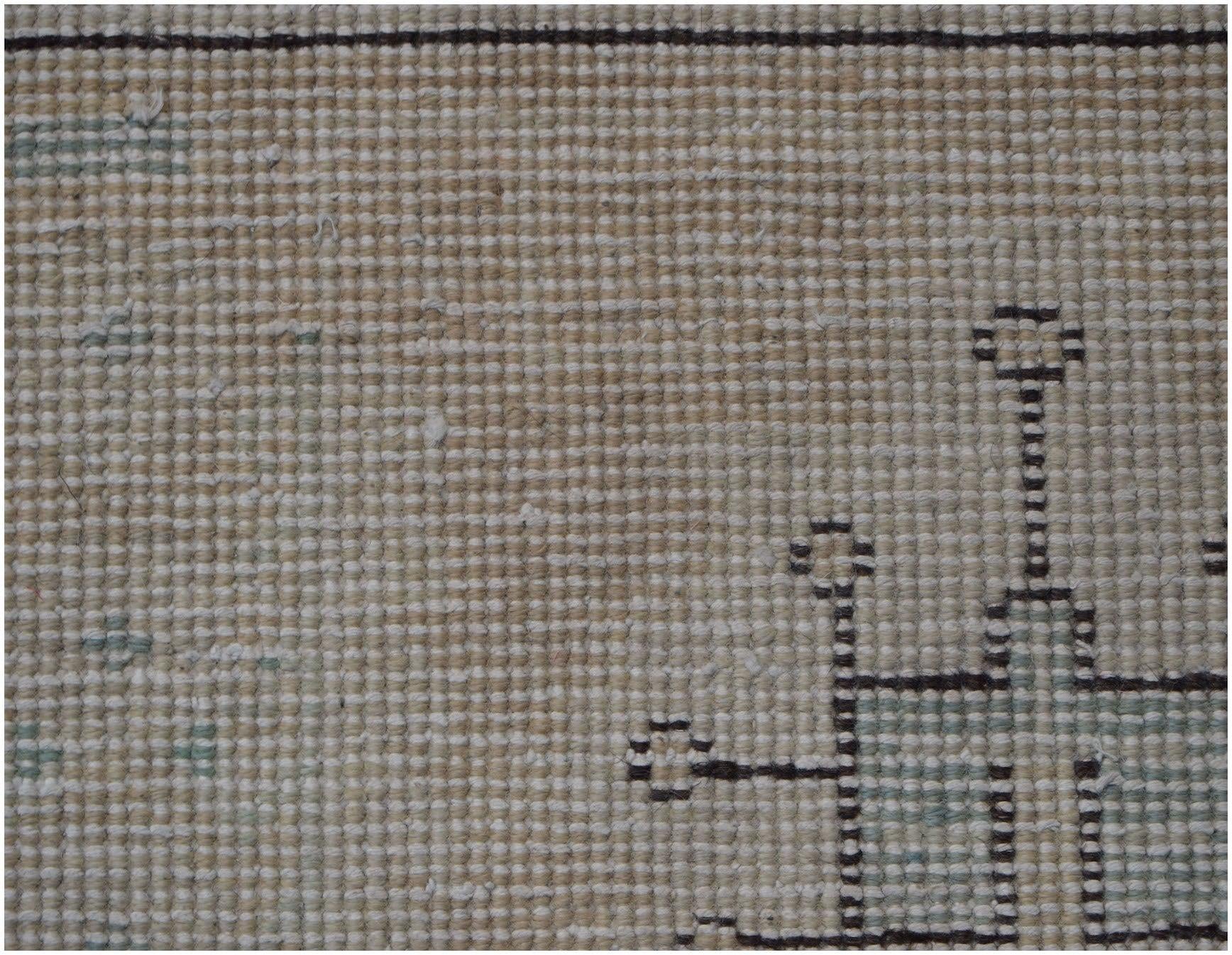 A close-up view of a vintage Persian Kerman rug featuring a geometric pattern on a beige field.