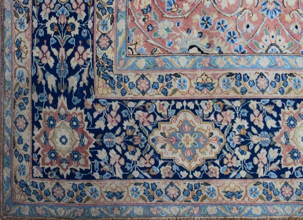 A vintage Persian Kerman rug featuring an intricate floral pattern in blue, pink, and cream tones.