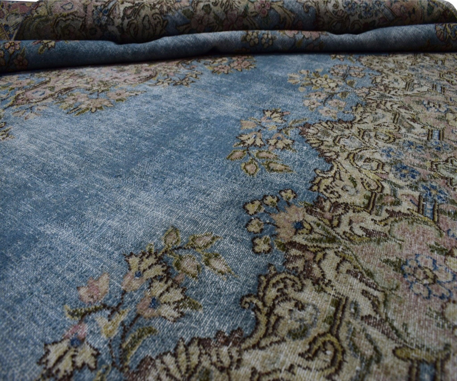 A vintage Persian Kerman rug featuring intricate floral patterns on a faded blue field.