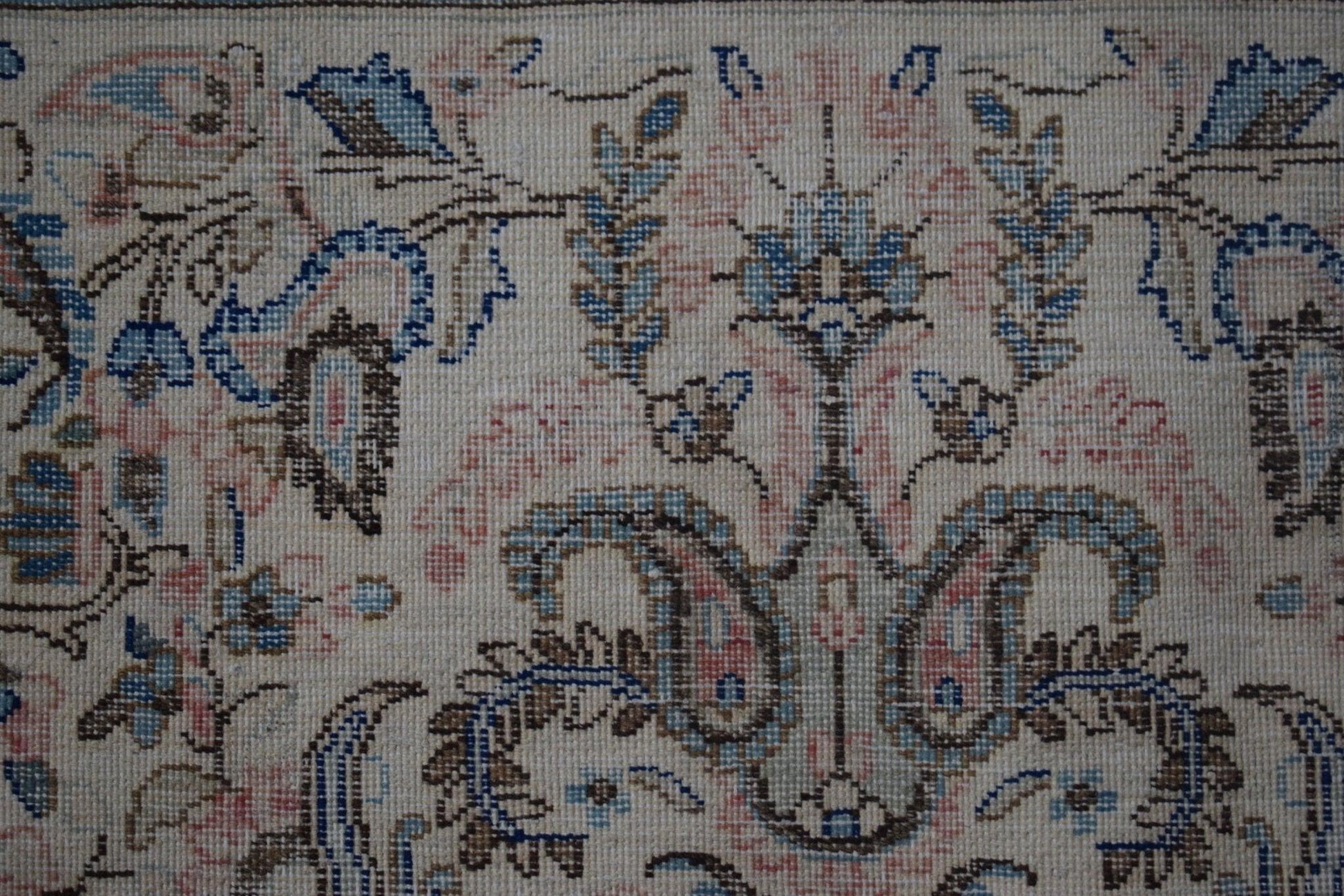 A close-up of a vintage Persian Kerman rug featuring intricate floral patterns in soft colors.