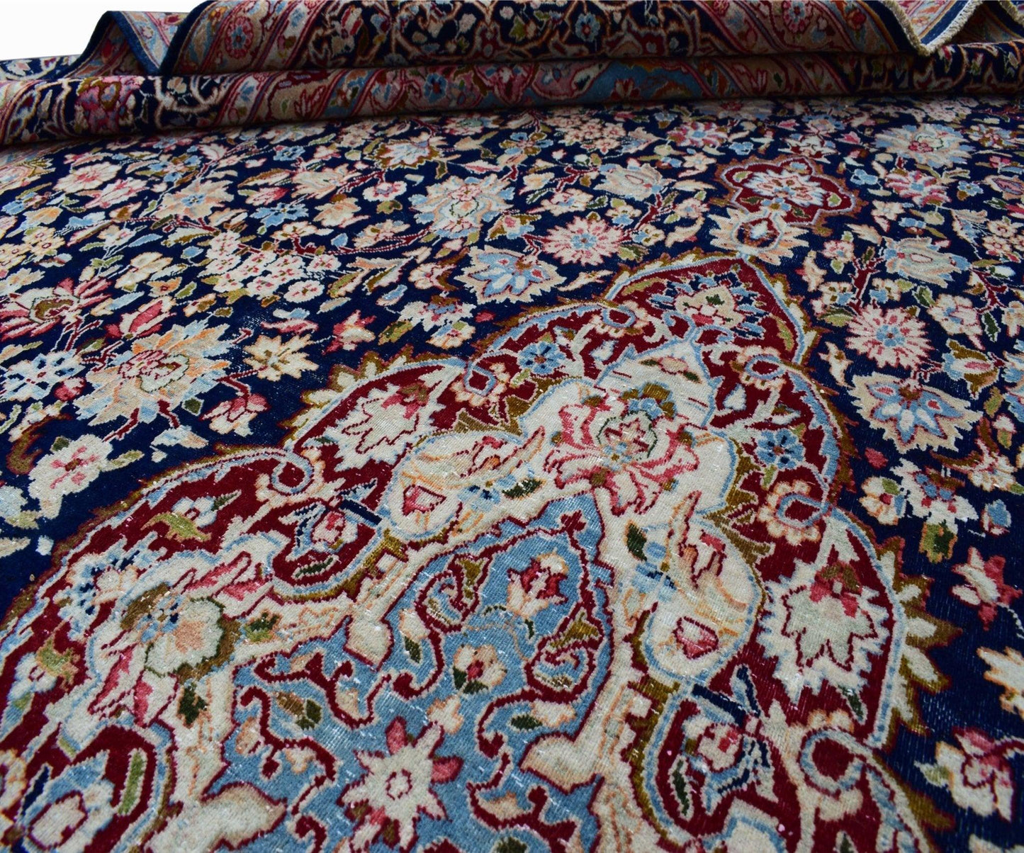 A vintage Persian Kerman rug featuring an intricate floral medallion on a deep blue background.