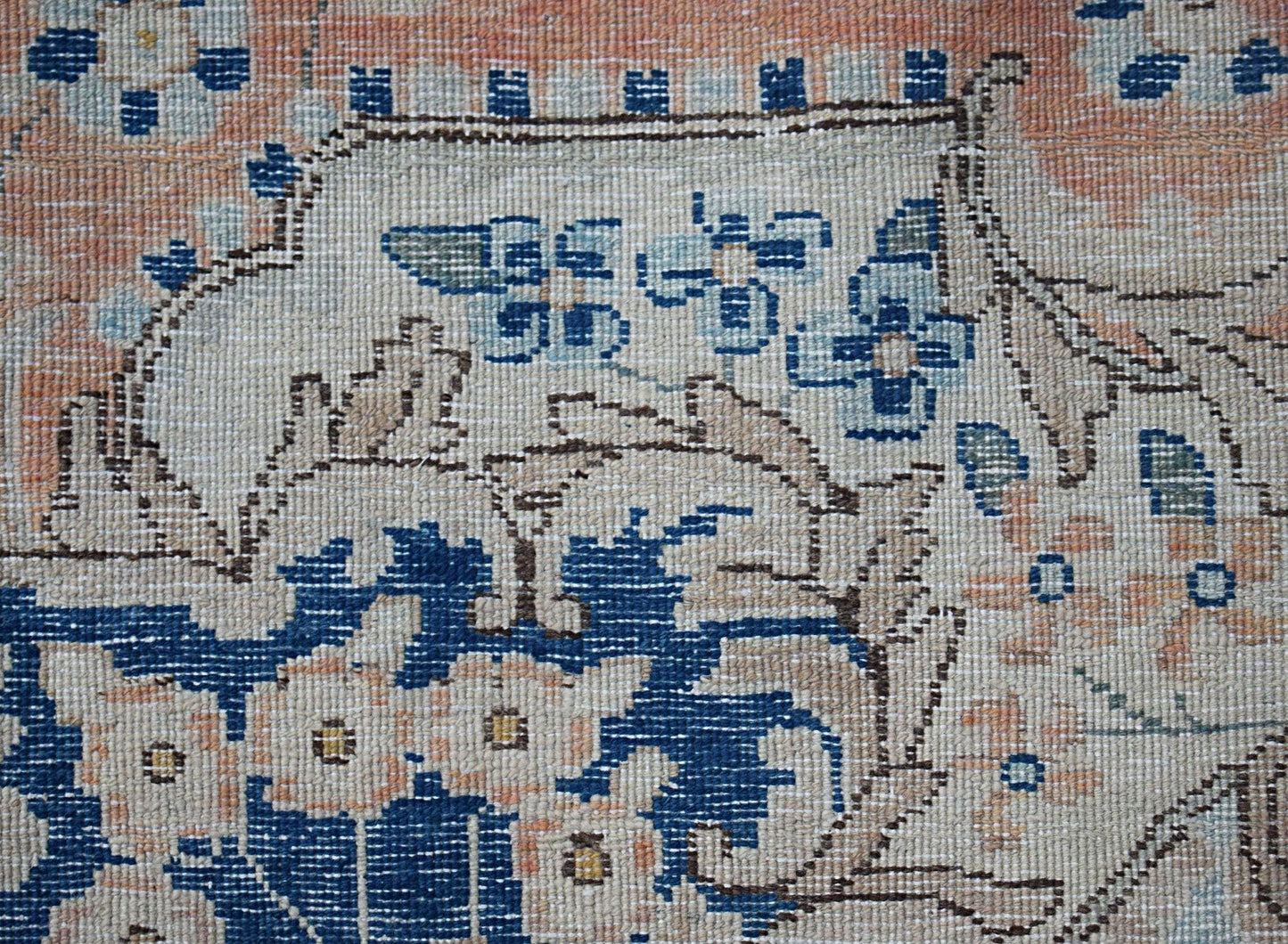 A close-up of a vintage Persian Kerman rug featuring intricate blue floral motifs on a cream field.