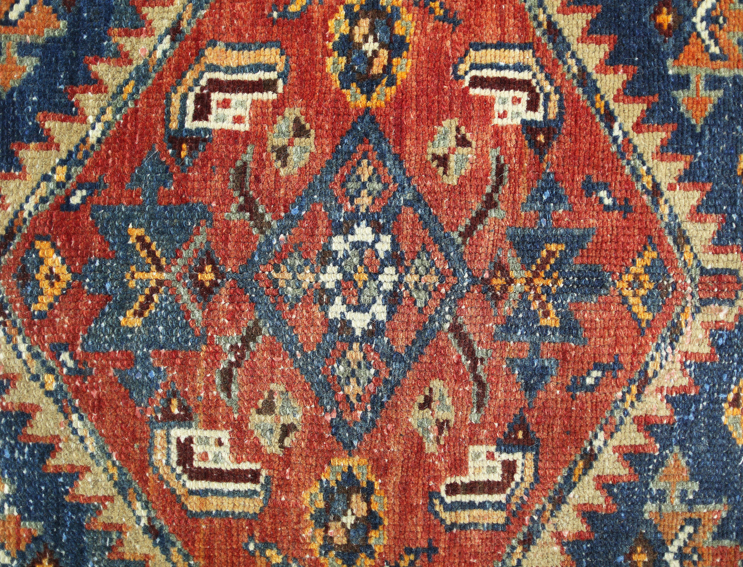 A vintage Persian rug featuring a central geometric diamond motif in red, blue, and cream tones.