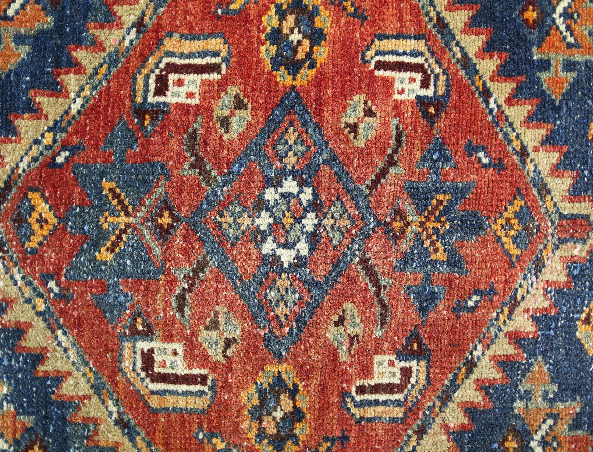 A vintage Persian rug featuring a central geometric diamond motif in red, blue, and cream tones.