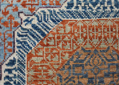 A close-up of a handwoven Afghan Balkh rug featuring intricate geometric patterns in blue and orange.