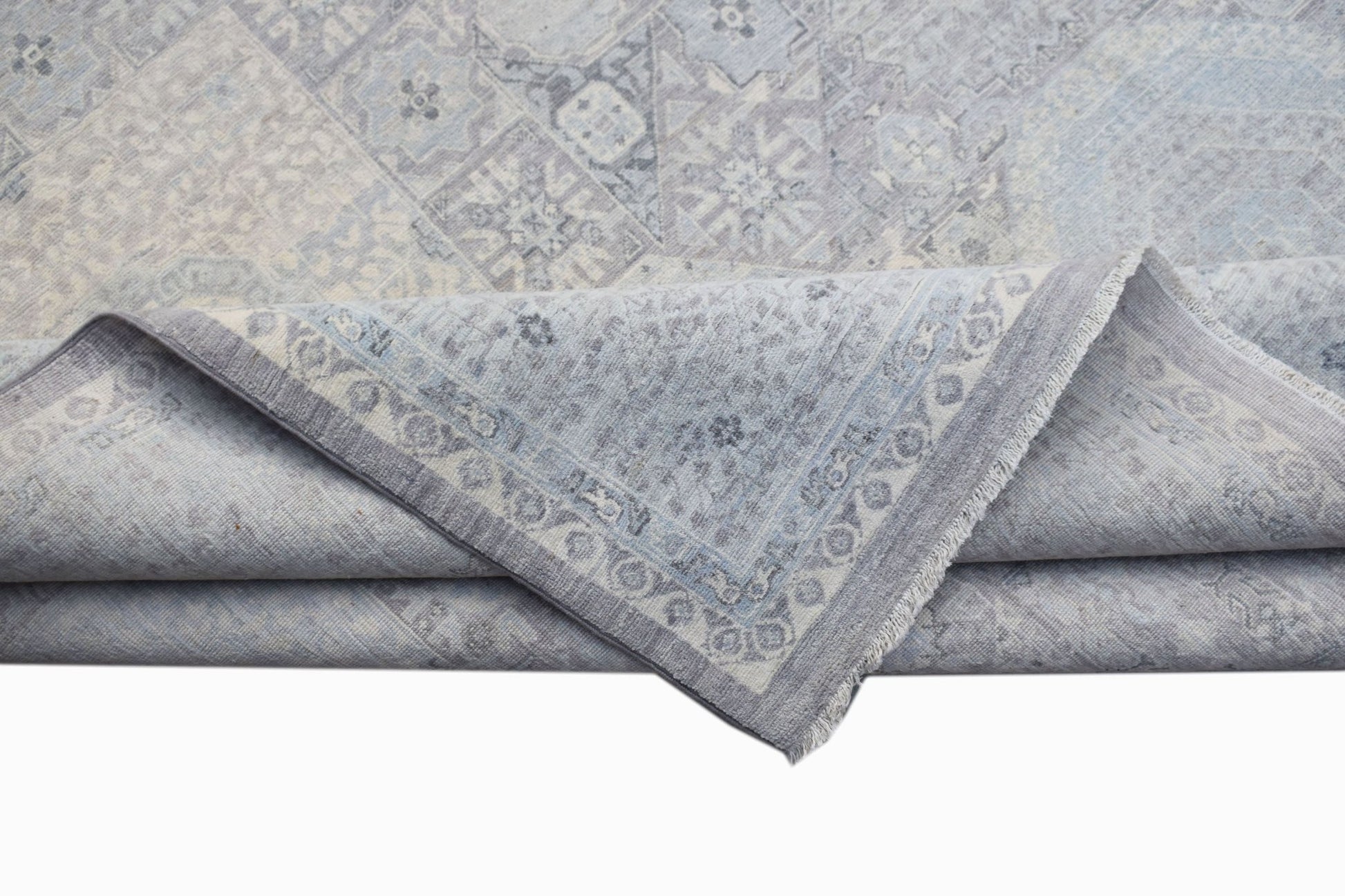 A handwoven Afghan Balkh rug in a light blue Mamluk pattern with a folded corner.