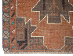 A handmade Afghan Baluch rug featuring geometric patterns in shades of brown and orange.