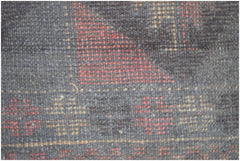 A close-up view of a handmade Afghan Baluch rug featuring geometric patterns in red and tan wool.