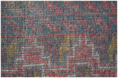 A close-up view of a handmade Afghan Baluch rug featuring geometric patterns in red, gold, and grey.