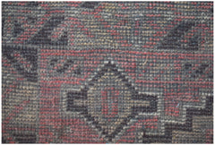 A close-up of a handmade Afghan Baluch rug featuring geometric diamond patterns in red and black.