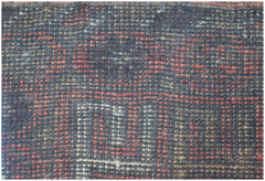 A close-up of a handmade Afghan Baluch rug featuring a geometric pattern in red, black, and tan.